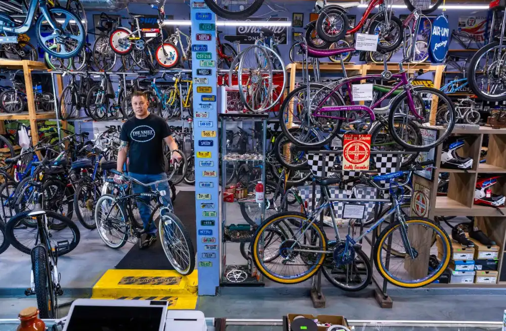 Owner Mike Skoy standing on the shop floor with a cruiser bike, surrounded by bicycles and a column covered in license plates