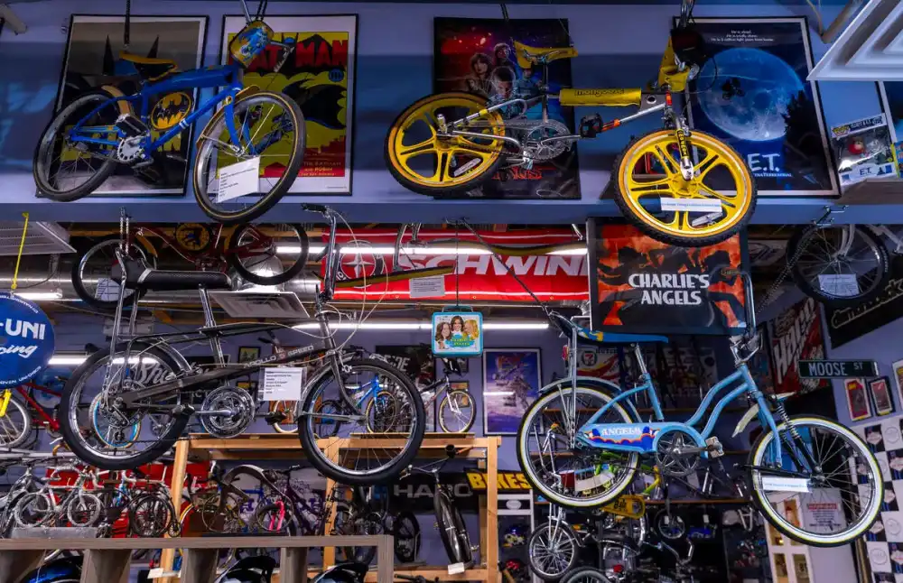 Museum wall at The Vault: a Batman-themed BMX beside its comic poster, a Mongoose with yellow mag wheels under an E.T. poster, a Charlie's Angels banner and rows of vintage bikes